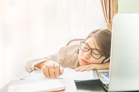 Teenage girl short hair sleep on desk after working on laptop while sit near window at home officeの写真素材