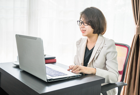 Young asian woman short hair in smart casual wear working on laptop while sitting near window in home officeの写真素材