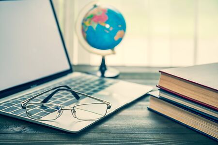 Eye glasses and book and simulated world with laptop on wooden table beside the windowの写真素材