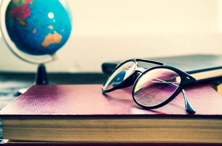 Eye glasses and books and simulated world on wooden table beside the windowの写真素材