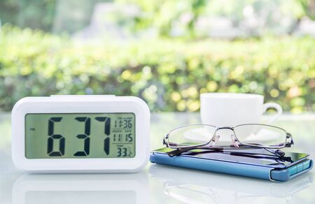 Close up Digital clock and eyeglass on table at office with coffee cupの写真素材