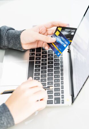 Online shopping concept. Close up of female hands holding plastic credit card and using laptop making online paymentの写真素材