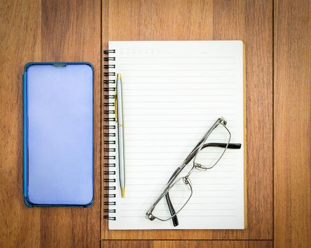 Top view image of open notebook with blank pages and cellphone ,eye glasse on wooden table background for adding text or mockupの写真素材