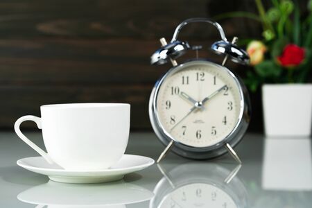 White coffee cup and alarm clock with Artificial flower vase bouquet on tableの写真素材