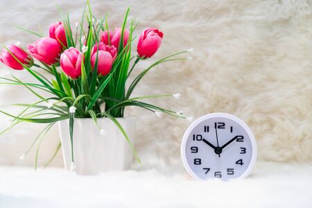 Close up white alarm clock with and flower bouquet in vase on tableの写真素材