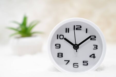 Close up white alarm clock and little decorative treein vase on table