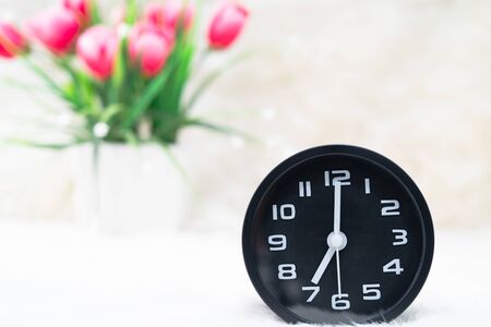 Close up Black alarm clock with and flower bouquet in vase on table