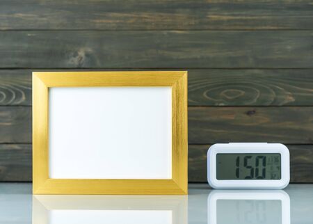 Mock up with blank golden frame and digital alarm clock on table with wood backgroundの写真素材