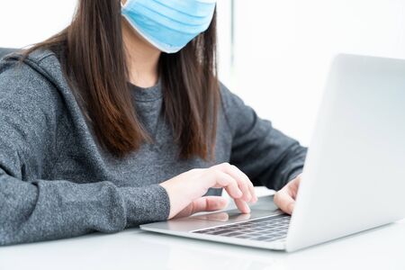 Woman using a laptop computer on the desk at home and wearing protective mask for protection against virus Covid-19の写真素材