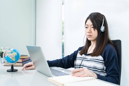 Young female student sitting in living room and learning online using laptop at desk .E-learning