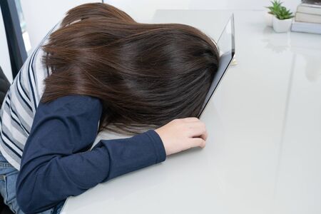 Young woman long hair tired from studying online and fall asleep on desk with laptopの写真素材