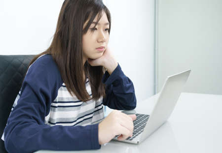 Young female student sitting in living room using laptop at desk learning onlineの写真素材