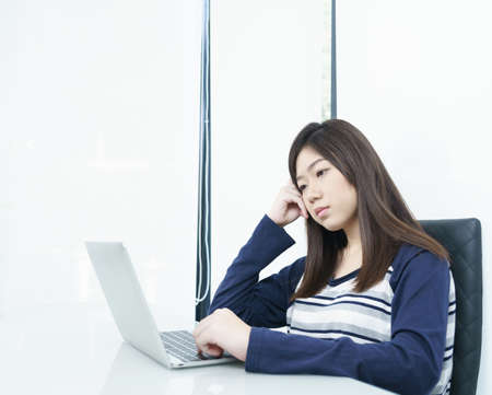 Young female student sitting in living room using laptop at desk learning onlineの写真素材