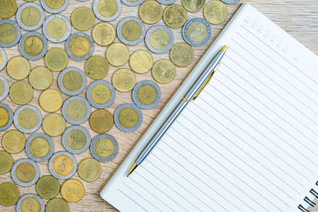 Top view coins with note pad on wood table using as financial concept