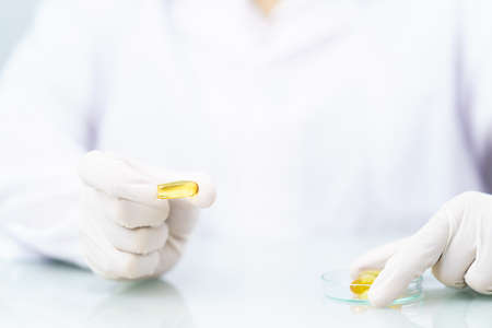 Close up Scientist hands putting in nitrile latex gloves holding Omega 3 capsule in labcoat doing...