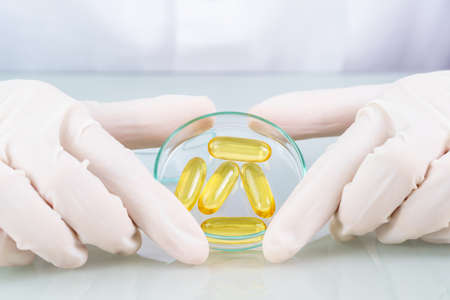 Close up Scientist hands putting in nitrile latex gloves holding Omega 3 capsule in labcoat wearing nitrile gloves, doing experiments in labの写真素材