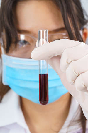 Technician scientist analyzing holding blood sample in test tube in laboratory for testing it on COVID, COVID-19, coronavirus virus analysisの写真素材