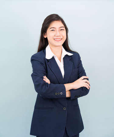 Teenage girl long hair is standing with her arms crossed wearing suit and white shirt on blue backgroundの写真素材