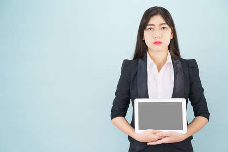 Young women in suit holding her digital tablet standing against blue backgroundの写真素材