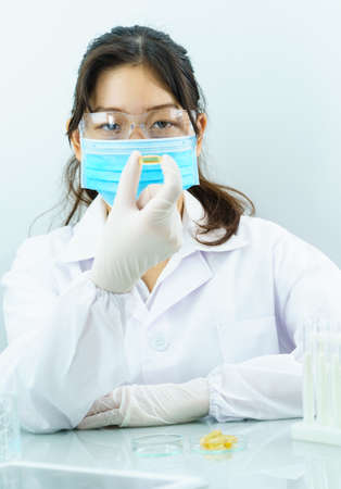 Close up Scientist hands putting in nitrile latex gloves holding Omega 3 capsule in labcoat doing experiments in labの写真素材