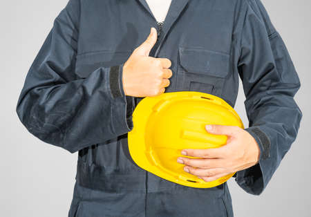 Cloes up Worker standing in blue coverall holding yellow hardhat isolated on gray backgroundの写真素材