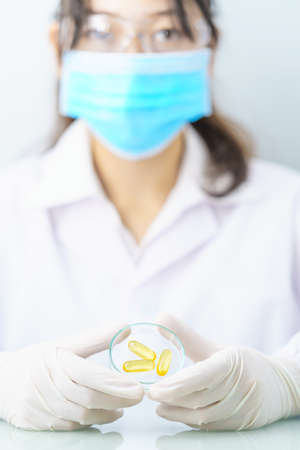 Close up Scientist hands putting in nitrile latex gloves holding Omega 3 capsule in labcoat doing experiments in labの写真素材