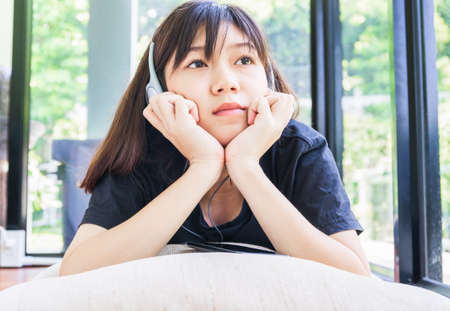 Teenage girl with headphones and listening to music from mobile phone at homeの写真素材