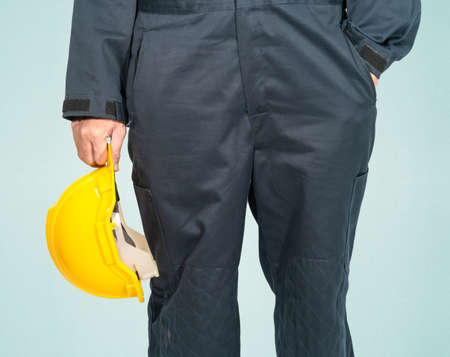 Worker standing in blue coverall holding yellow hardhat isolated on blue backgroundの写真素材