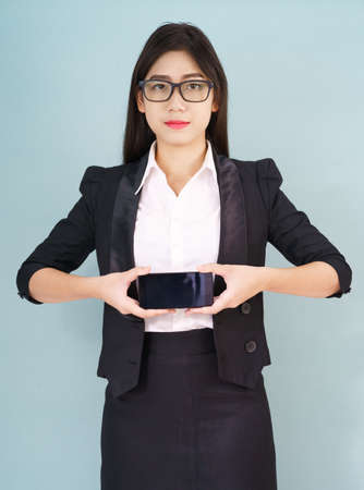 Young women in suit holding her smartphone standing against blue backgroundの写真素材