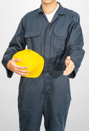 Worker standing in blue coverall holding yellow hardhat isolated on gray backgroundの写真素材
