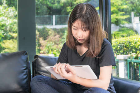 Young girl studying online from digital tablet on the sofa in parlor at homeの写真素材
