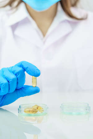 Close up Scientist hands putting in nitrile blue latex gloves holding Omega 3 capsule in lab coat wearing nitrile glovesの写真素材