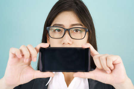 Young women in suit holding her smartphone standing against blue backgroundの写真素材
