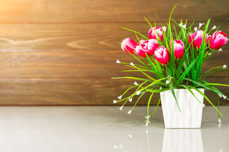 Artificial flower vase bouquet over table against wooden wallの写真素材