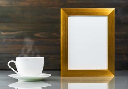 Picture mock up with golden frame and coffee cup over table with wood wall backgroundの写真素材