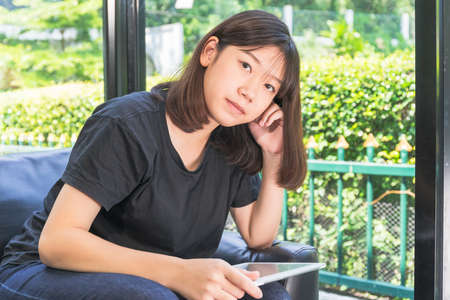 Young girl studying online from digital tablet on the sofa in parlor at homeの写真素材