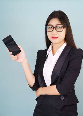 Young women in suit holding her smartphone standing against blue backgroundの写真素材