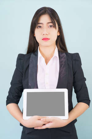 Young women in suit holding her digital tablet standing against blue backgroundの写真素材