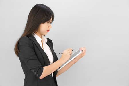 Young women in suit using her digital tablet standing against gray backgroundの写真素材