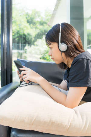 Young girl with headphones and listening to music from mobile phone on the sofa in living room at homeの写真素材