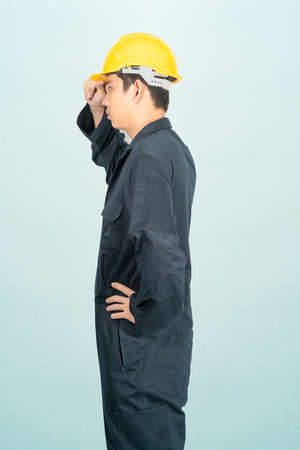 Young man in coveralls helmet hardhat isolated on blue backgroundの写真素材
