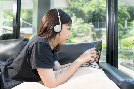 Young girl with headphones and listening to music from mobile phone on the sofa in living room at homeの写真素材