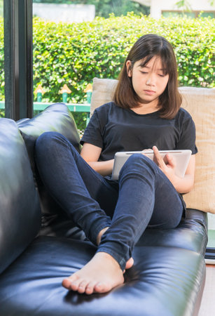 Young girl studying online from digital tablet on the sofai n living room at homeの写真素材