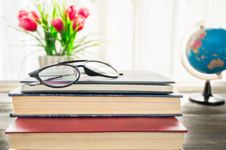 Reading glasses put on hardcover books over wooden table beside the windowの写真素材