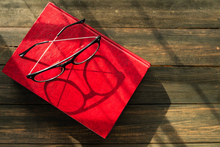Reading glasses put on hardcover books over wooden tableの写真素材