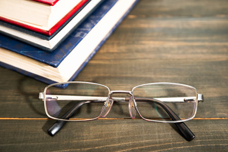 Glasses and stack of hardcover books over wooden tableの写真素材