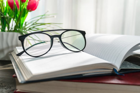 Reading glasses put on open books over wooden table beside the windowの写真素材