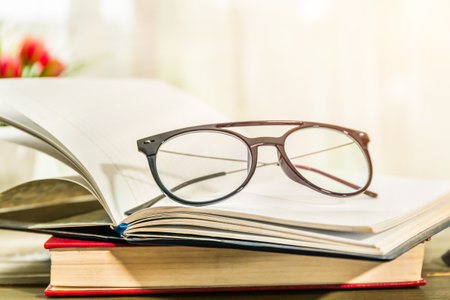 Reading glasses put on open books over wooden table beside the windowの写真素材