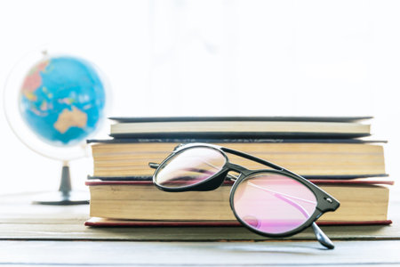 Reading glasses put on hardcover books over wooden tableの写真素材