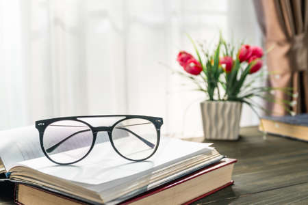 Reading glasses put on open books over wooden table beside the window